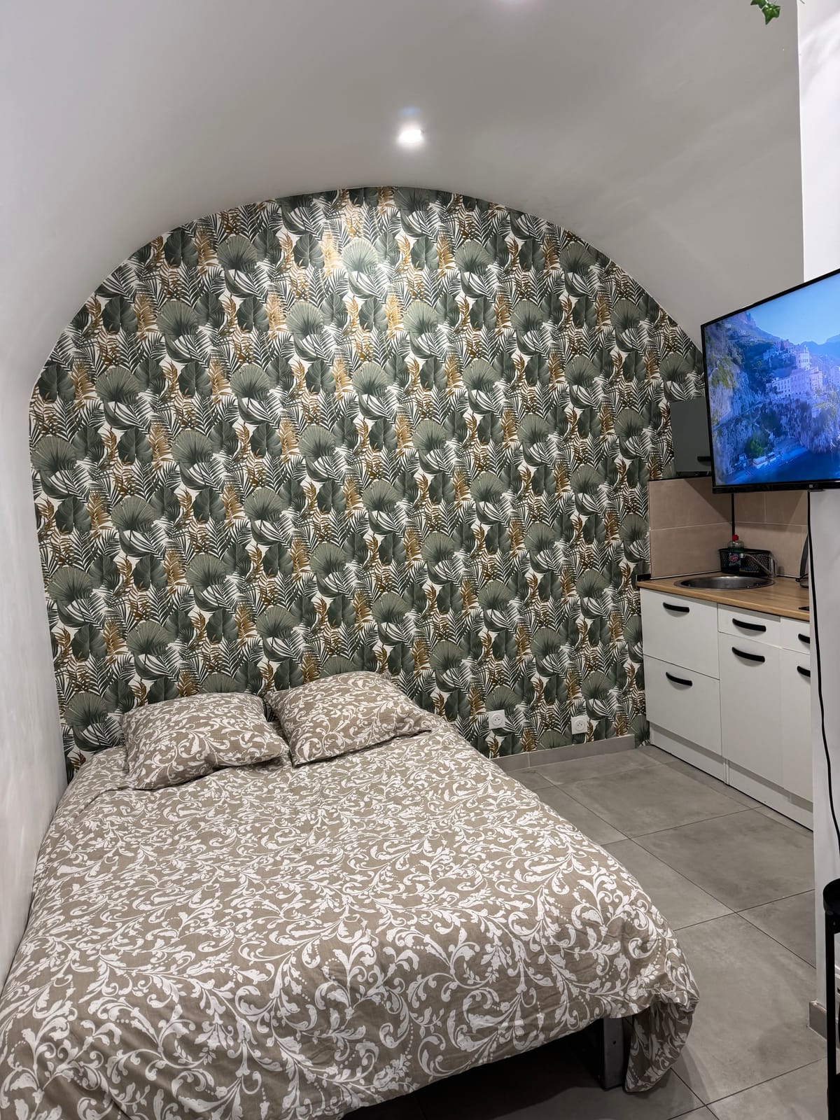 Doppelbett unter der gewölbten Nische mit Blatttapete, Küchenzeile im Hintergrund